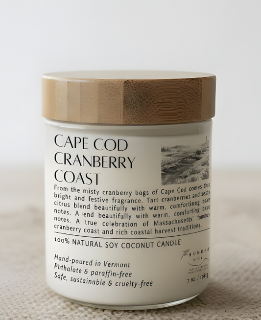 A soy coconut candle jar labeled 'CAPE COD CRANBERRY COAST' by The BONDed Wick with a white body, black text, a light wood lid, and a soft neutral background.